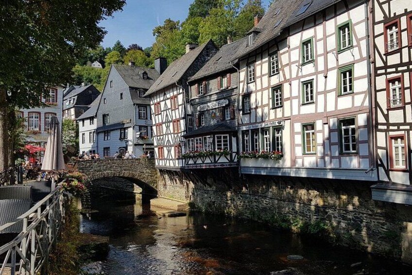 A historic town with a stone bridge over a river, traditional half-timbered houses, and a statue in the foreground. 2