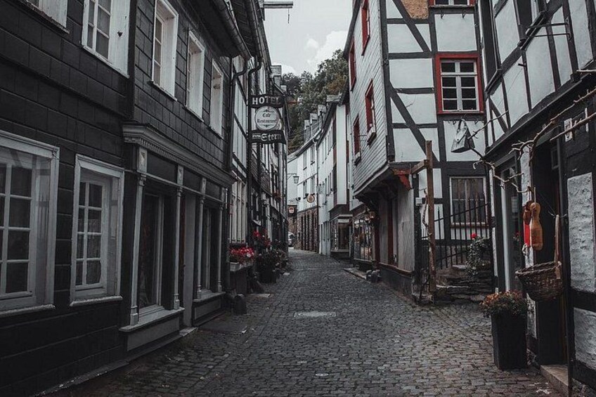 A cobblestone street lined with traditional half-timbered buildings, a sign for a hotel, and a small shop with flowers. 1