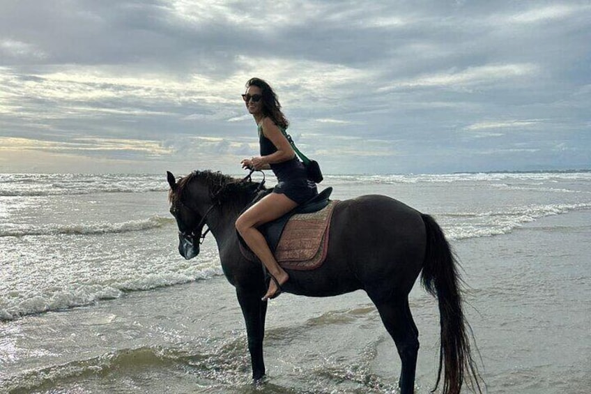 En person som rider på en häst på en strand, med vågor i bakgrunden. 3