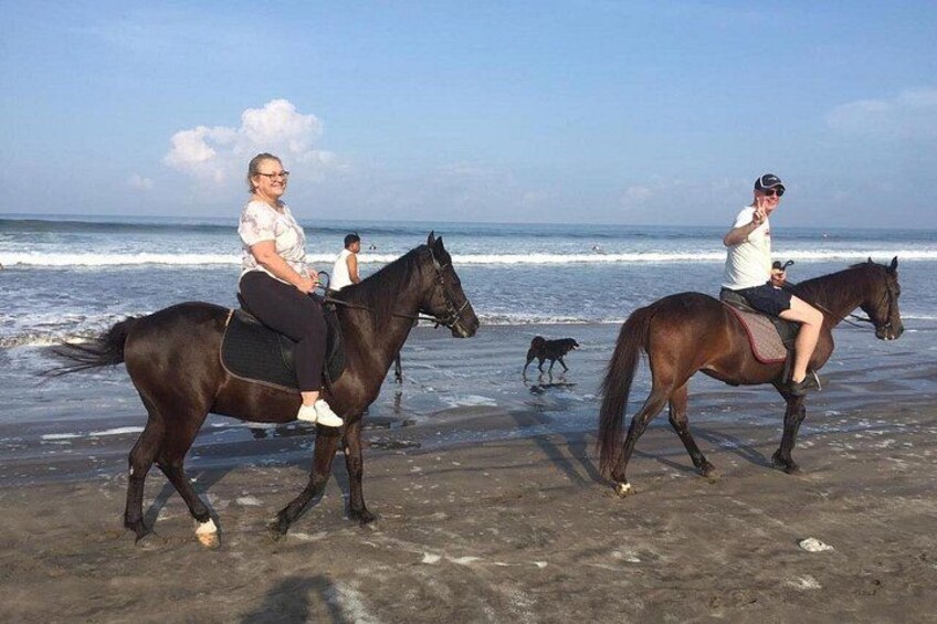 Dos personas cabalgando caballos en una playa con el océano al fondo. 2