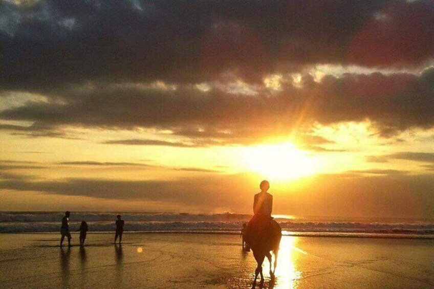 Un atardecer sobre una playa con gente caminando y una persona montando a caballo. 3