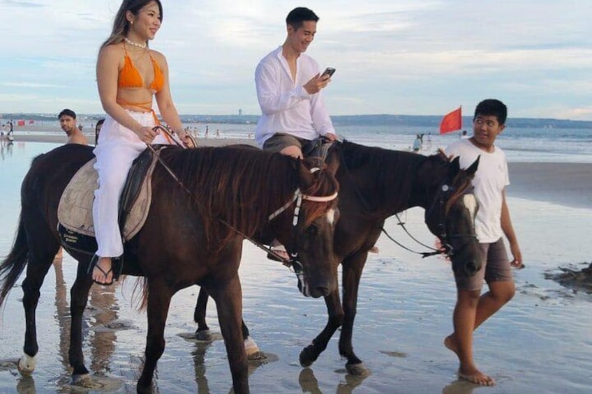 Dos caballos en la playa con gente montándolos y paseándolos. 2
