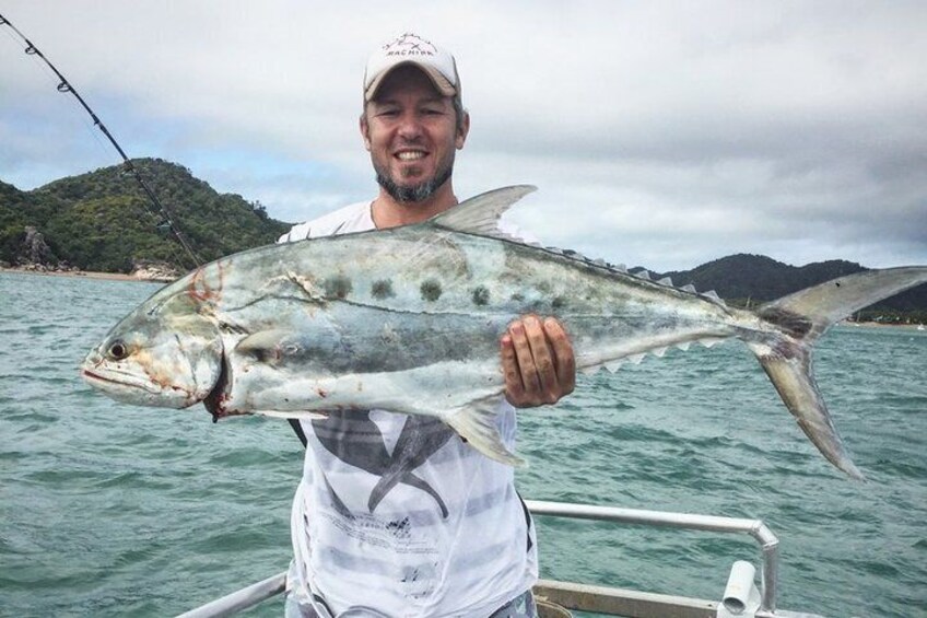 A person holding a large fish on a boat with a mountainous landscape in the background. 4