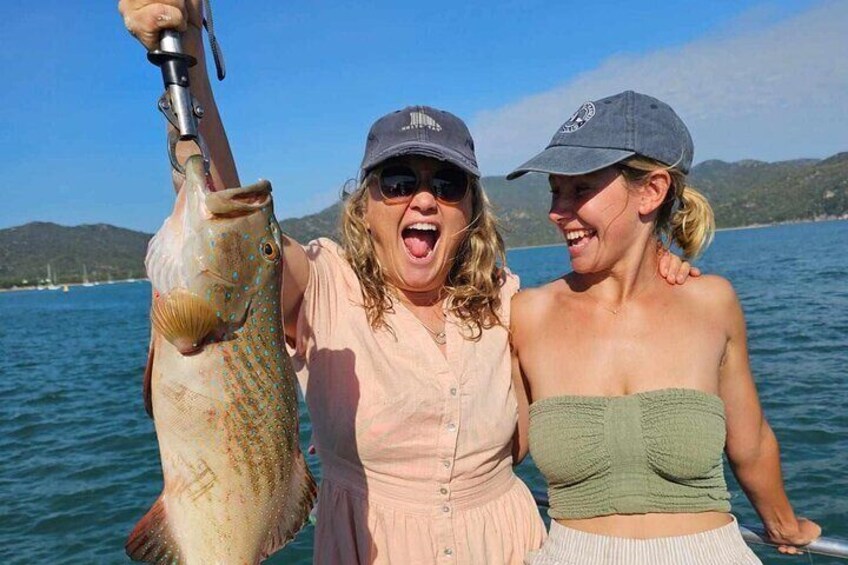 Two people holding a large fish on a boat with a lake and hills in the background. 3