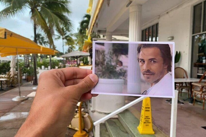 A hand holding a photo card with a blurred face, palm trees, outdoor seating, and a yellow umbrella in the background. 3
