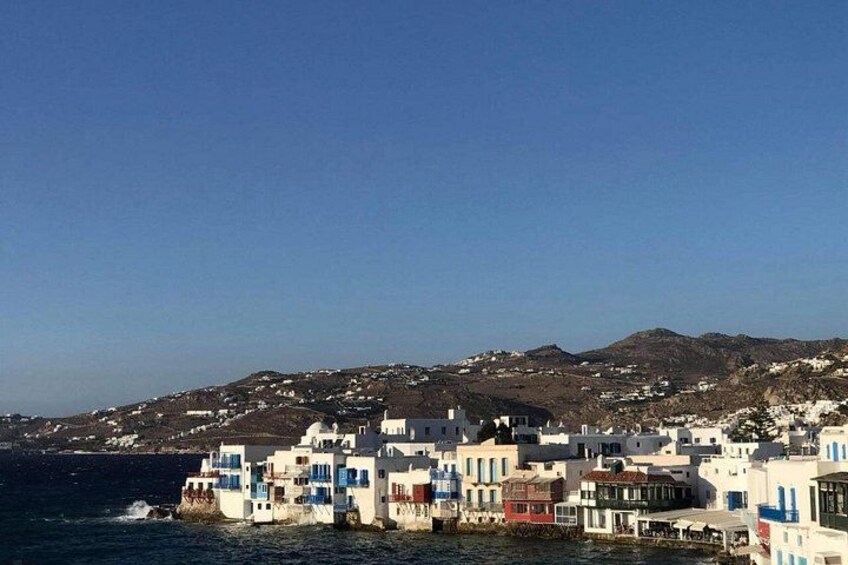 A coastal village with white buildings, a clear blue sky, and a hilly background. 2