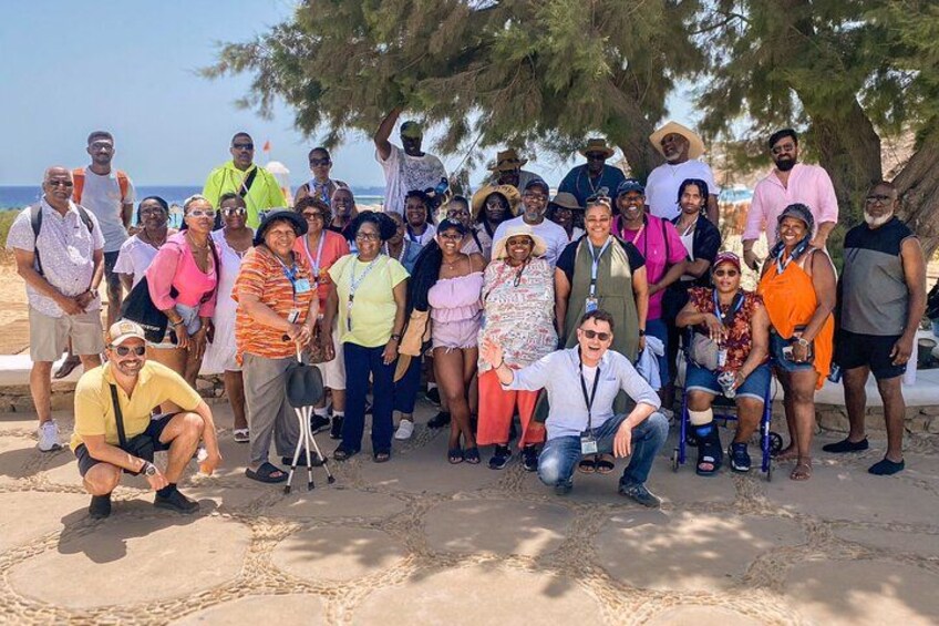 Un grupo de personas posando para una foto en una playa arenosa, con árboles y el océano al fondo. 2