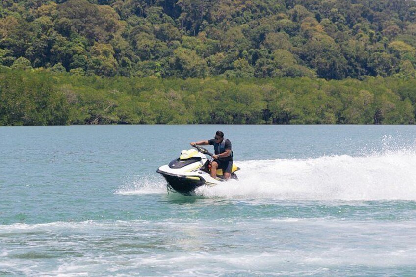 A person riding a jet ski on a body of water with a forested shoreline in the background. 3