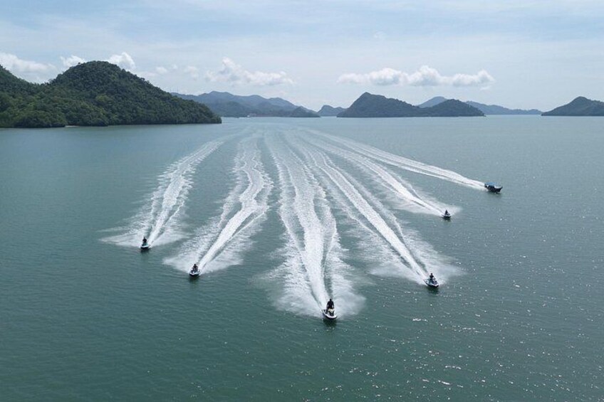 A group of jet skis creating wake trails on a calm lake with mountains in the background. 2