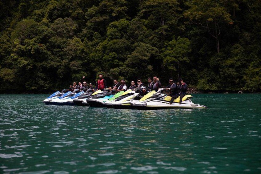 A group of people on jet skis on a lake surrounded by dense forest. 5