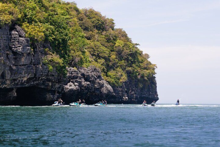 Eine felsige Klippe mit dichter, grüner Vegetation, mehrere kleine Boote im Wasser und ein Jetski. 5