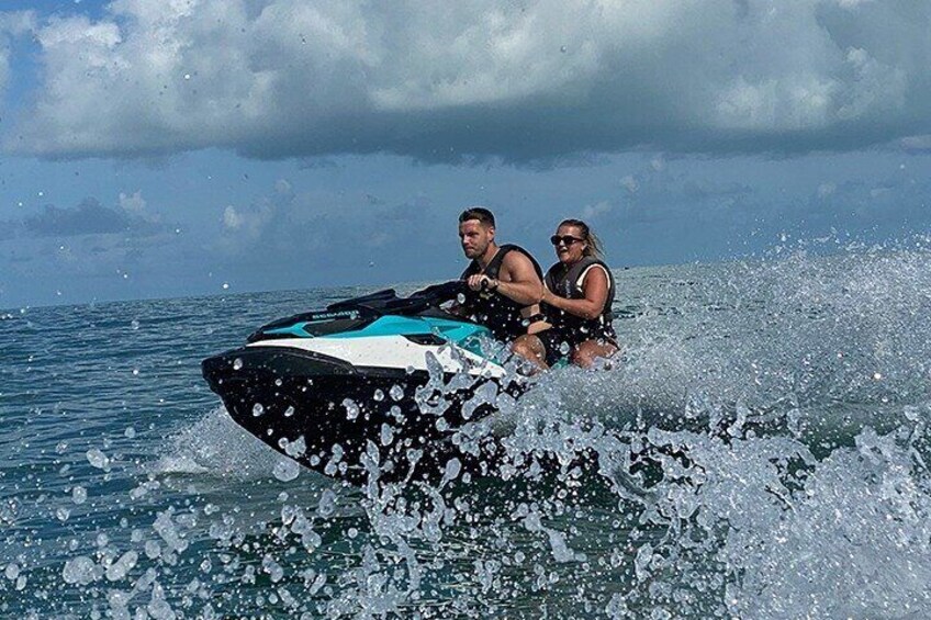 Zwei Personen fahren mit Jet-Skis über das Wasser, dabei spritzen Wassertropfen herum. 1