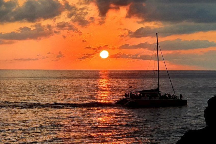 A sunset over the ocean with a boat and a rocky shoreline. 3