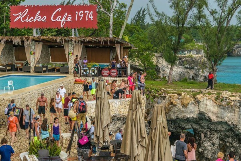 Un café frente a la playa con terraza, piscina y gente relajándose. 2