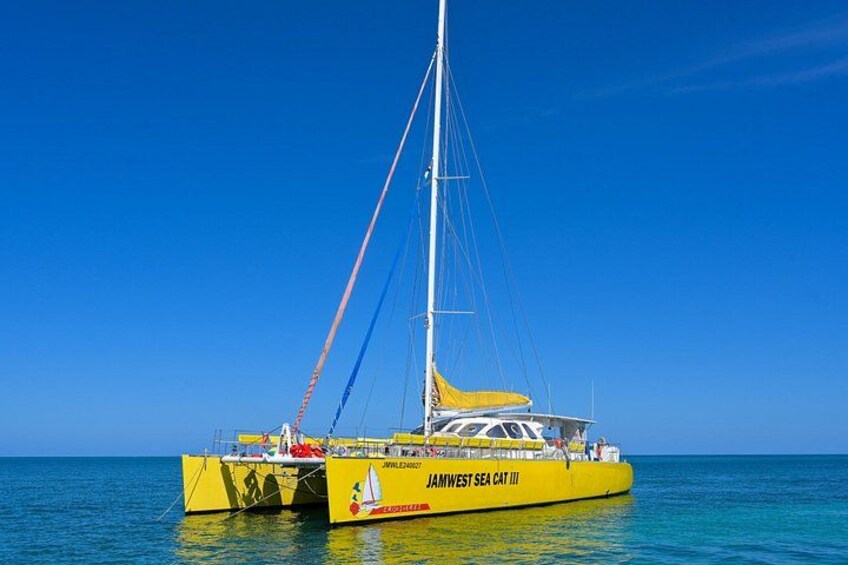Un catamarán amarillo llamado 'JAMWEST SEA CAT III' sobre aguas tranquilas. 1