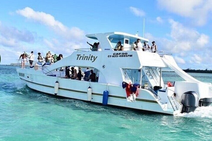 A white boat named Trinity with people on board, moving through clear blue water. 3