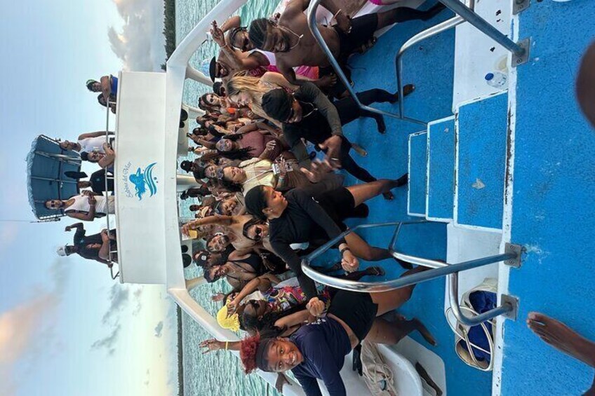 A group of people on a boat with a blue deck, some wearing hats and sunglasses. 5