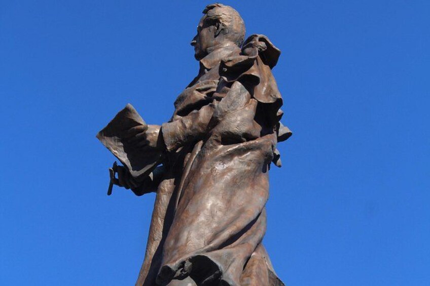 A bronze statue of a man holding a book and a cross. 2