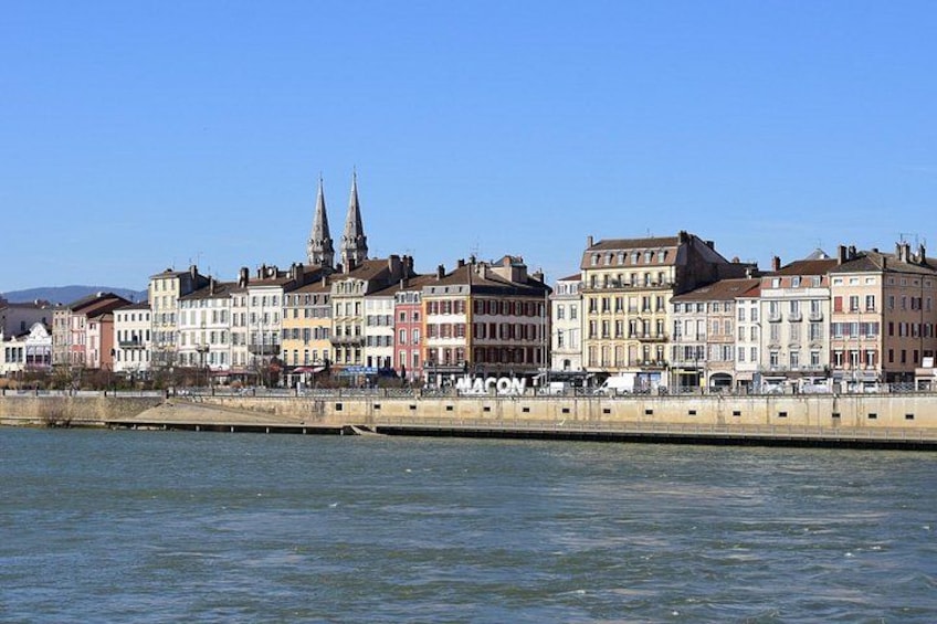 A riverside cityscape with historic buildings and two prominent church spires. 5