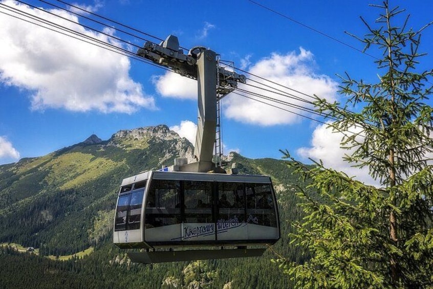 A cable car suspended over a mountainous landscape with lush greenery and a clear sky. 2