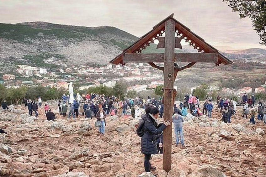 A rocky landscape with a wooden structure, possibly a monument, and a crowd of people in the background. 2