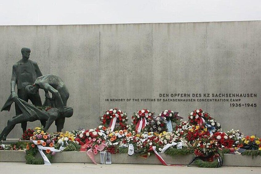 A memorial wall with a statue and floral tributes. 1