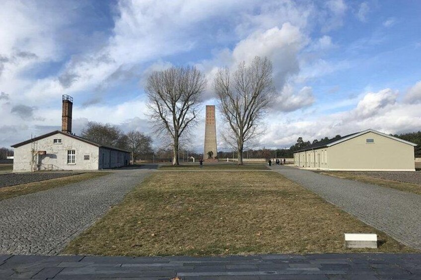 A grassy area with a tall monument, two buildings, and a clear sky. 2
