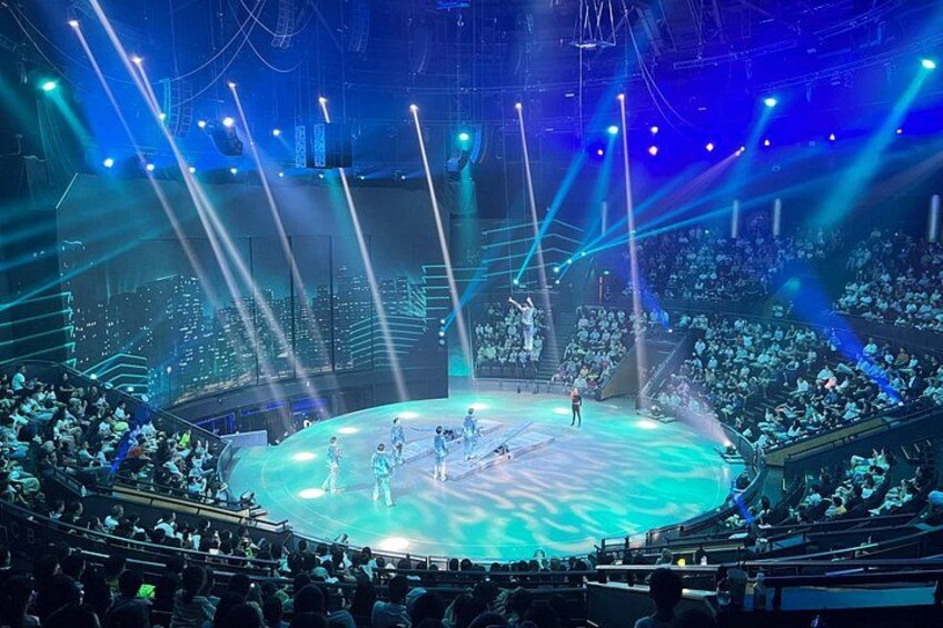 En stor inomhusarena med en scen, sittplatser för publiken och scenbelysning. 5