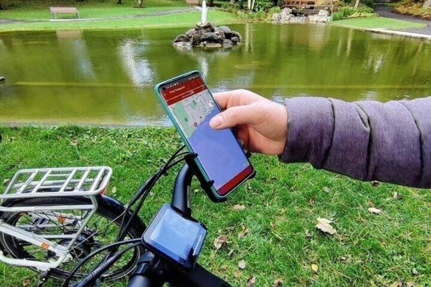 Une main tenant un smartphone avec une application de cartographie, un vélo avec un panier et, au fond, un étang avec une fontaine. 4