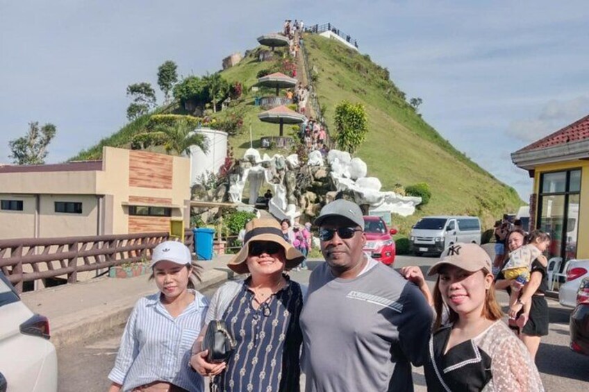 A group of people standing in front of a hill with a statue and a staircase. 4