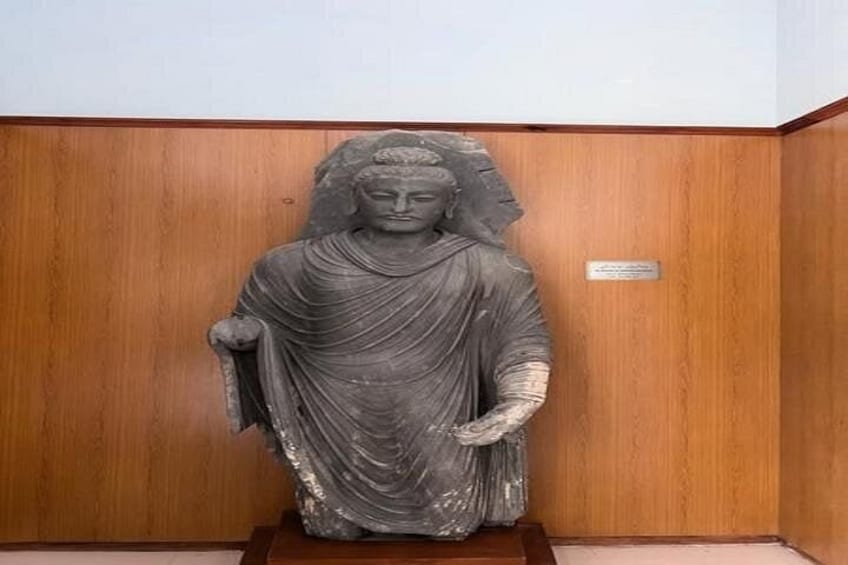 Una estatua de piedra de una figura sentada con túnica, ubicada frente a un fondo de paneles de madera. 5