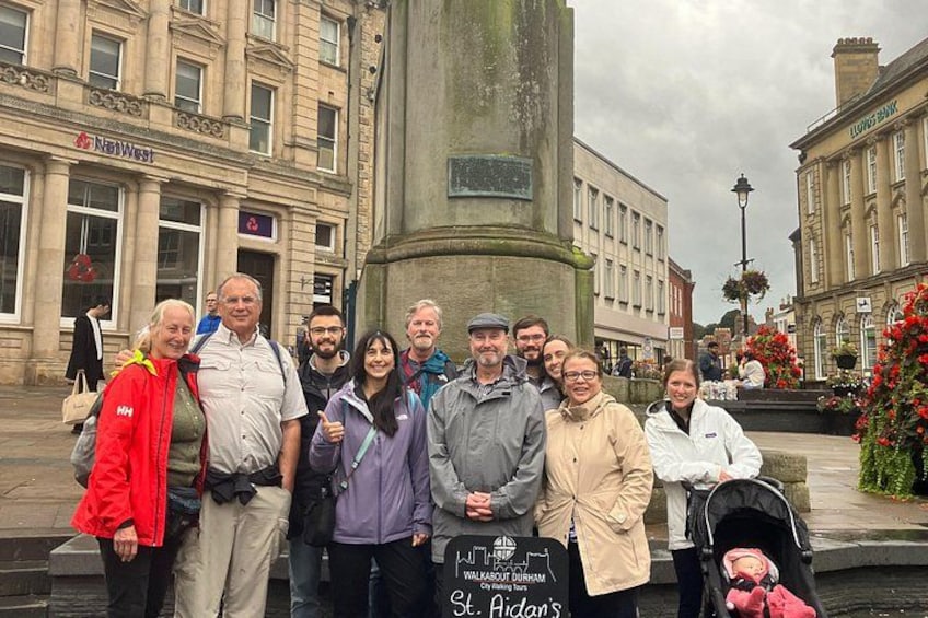 Un groupe de personnes posant devant un bâtiment historique, sur lequel on peut voir une plaque commémorative, une poussette et un panneau indiquant l’église Saint-Aidan. 4