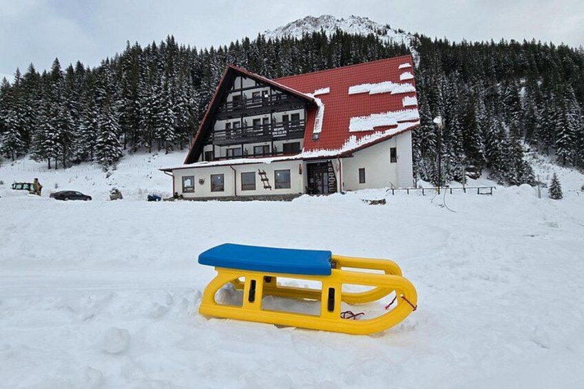 A snow-covered landscape with a red-roofed building and a yellow sled in the foreground. 2