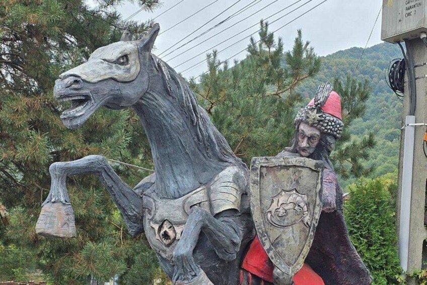 A statue of a horse and rider in armor, set against a backdrop of trees and a mountainous landscape. 5