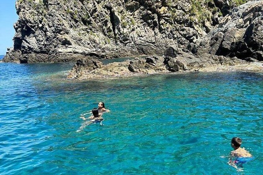 Dos personas nadando en agua azul cristalina, con acantilados rocosos al fondo. 2