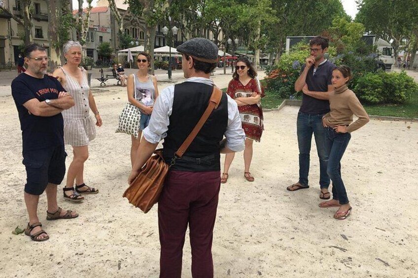 Un grupo de personas de pie en una zona arenosa, con edificios y árboles al fondo. 1