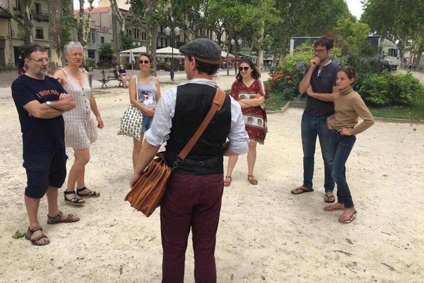 A group of people standing on a sandy area with trees and buildings in the background. 1