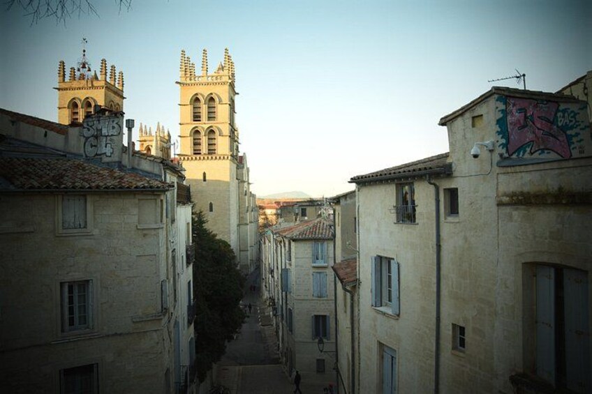 A narrow street flanked by old buildings, a church with a bell tower, and graffiti on a wall. 3