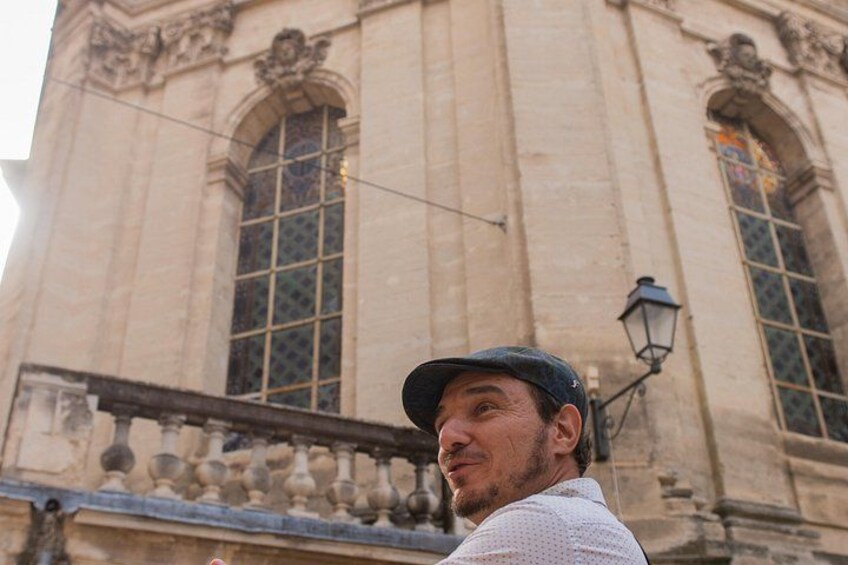 A person standing in front of a historic building with large windows and ornate architectural details. 5