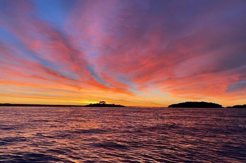A sunset over a body of water with a silhouette of a landmass in the distance. 2