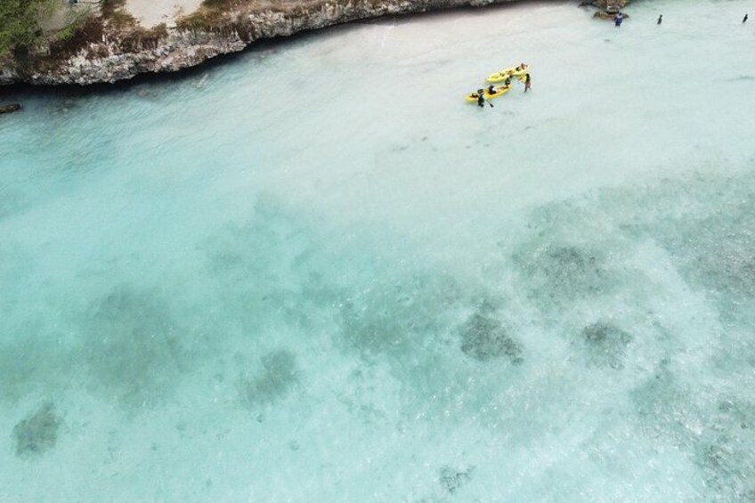 A beach with clear turquoise water, a rocky shoreline, and a group of people in yellow kayaks. 2