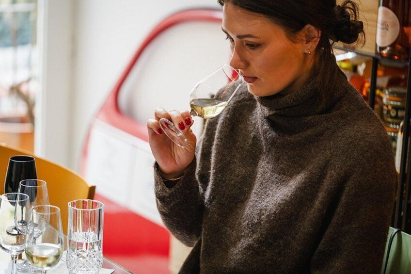 A person holding a wine glass, seated at a table with glasses and bottles. 4