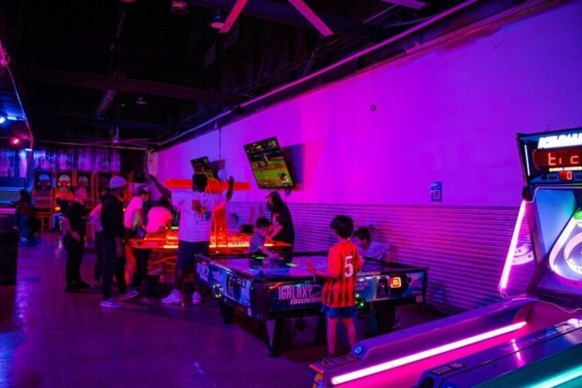 Un salón recreativo con luces de neón y personas jugando al tenis de mesa. 3