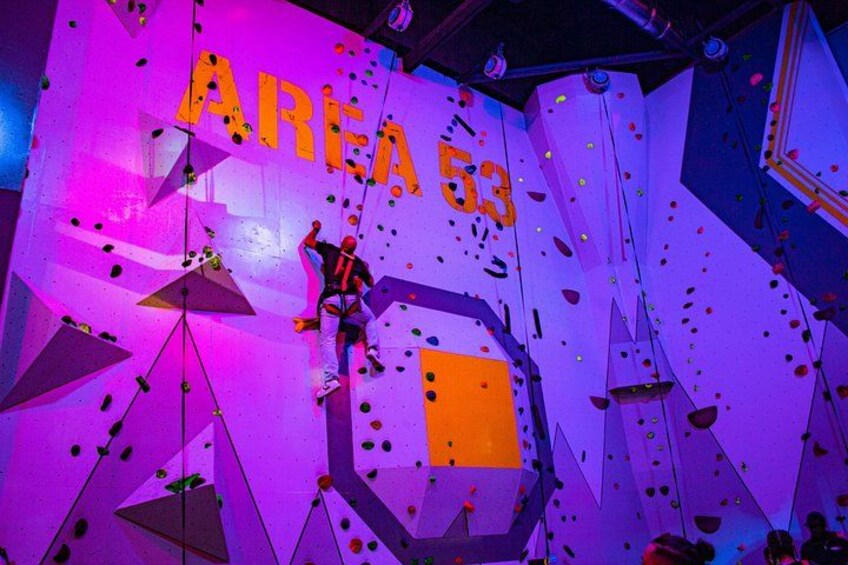 Una pared de escalada con el texto 'AREA 53' y diversas formas geométricas. 4