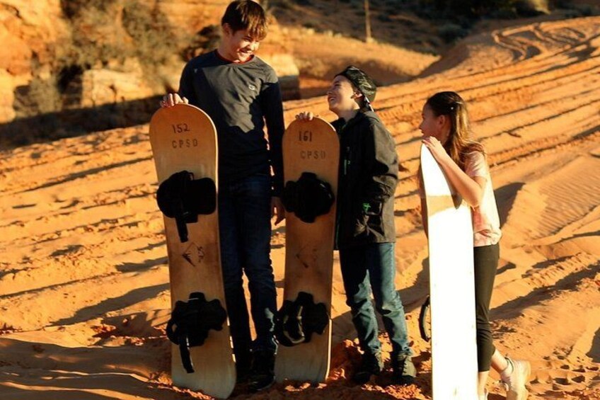 Three people standing on a sandy terrain with snowboards. 4