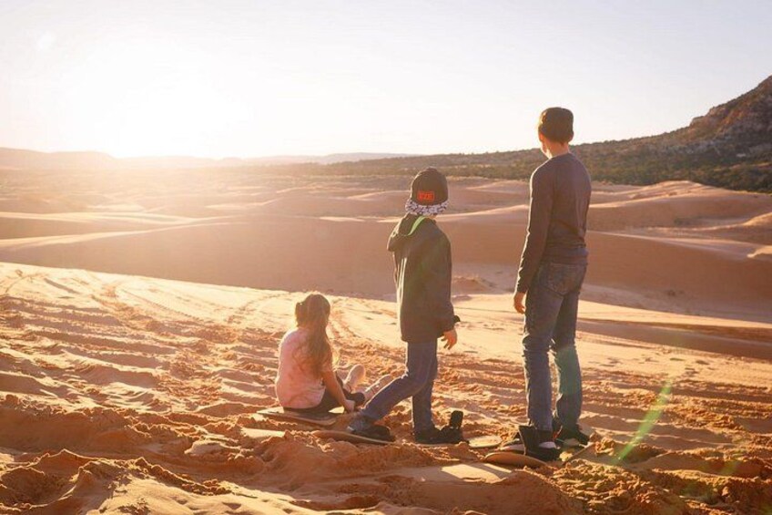 Three people in a desert landscape with sand dunes and a sunset. 2