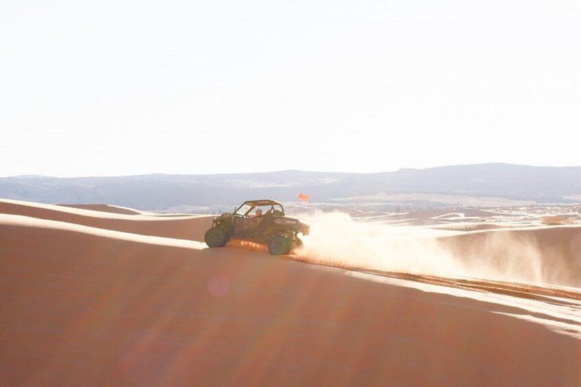 A vehicle driving on a sandy terrain with hills in the background. 2