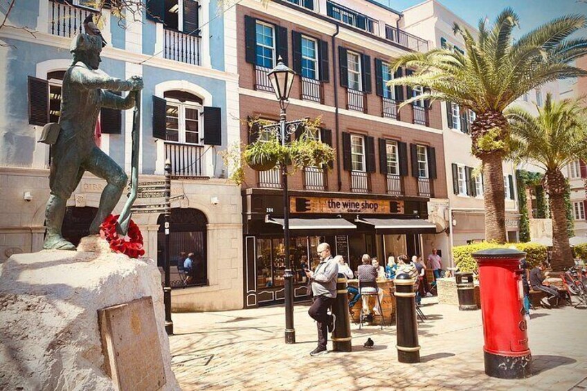 Una estatua de un hombre sosteniendo una pala, una tienda de vinos y gente sentada afuera. 5