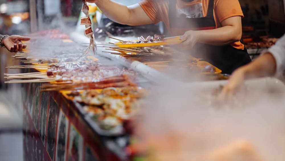 A food stall with skewers of meat and vegetables being grilled. 3