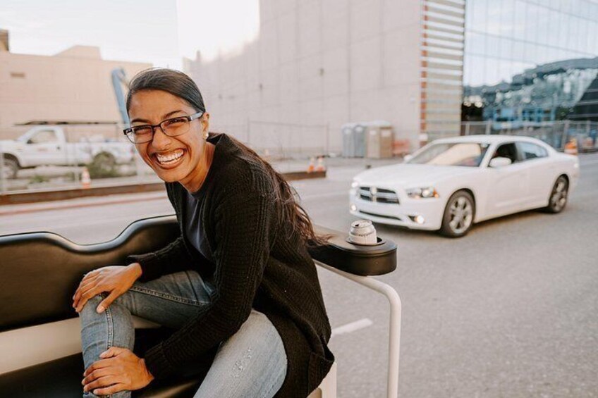 Una persona sentada en un banco con un coche blanco y un edificio al fondo. 2